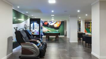 Mesa de bilhar em um espaço com cadeiras de massagem e um mural com tema de jogos de bilhar.