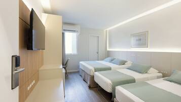 Quarto de hotel com duas camas, televisão na parede, janela com ar condicionado e uma porta.