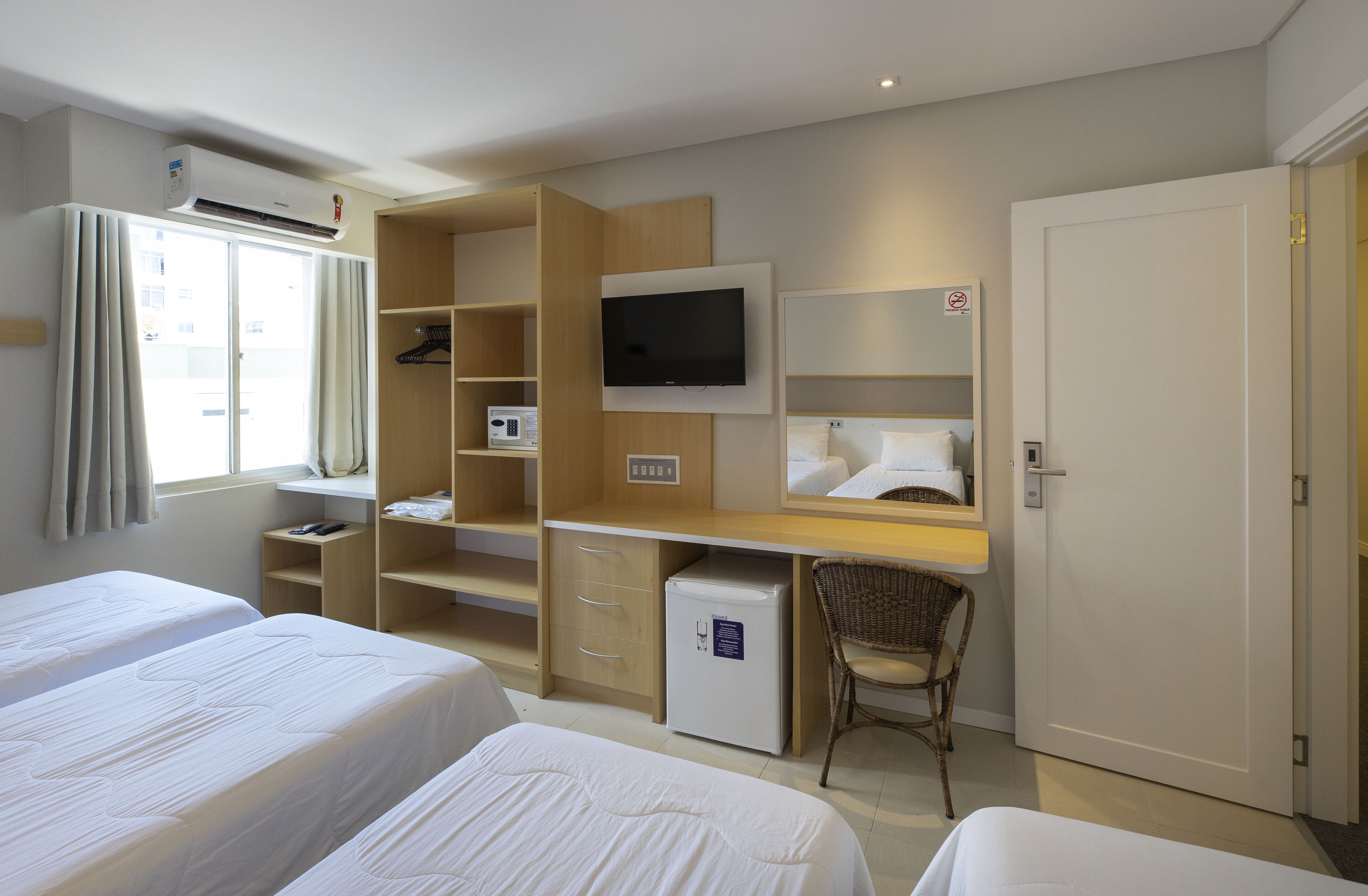 Une chambre d’hôtel avec deux lits, un bureau avec une télévision, un petit réfrigérateur, un four à micro-ondes et une armoire.