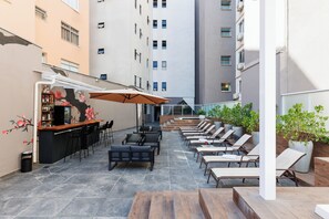 An outdoor seating area with a bar, lounge chairs, and potted plants. - Hotel Miramar (Balneário Camboriú)