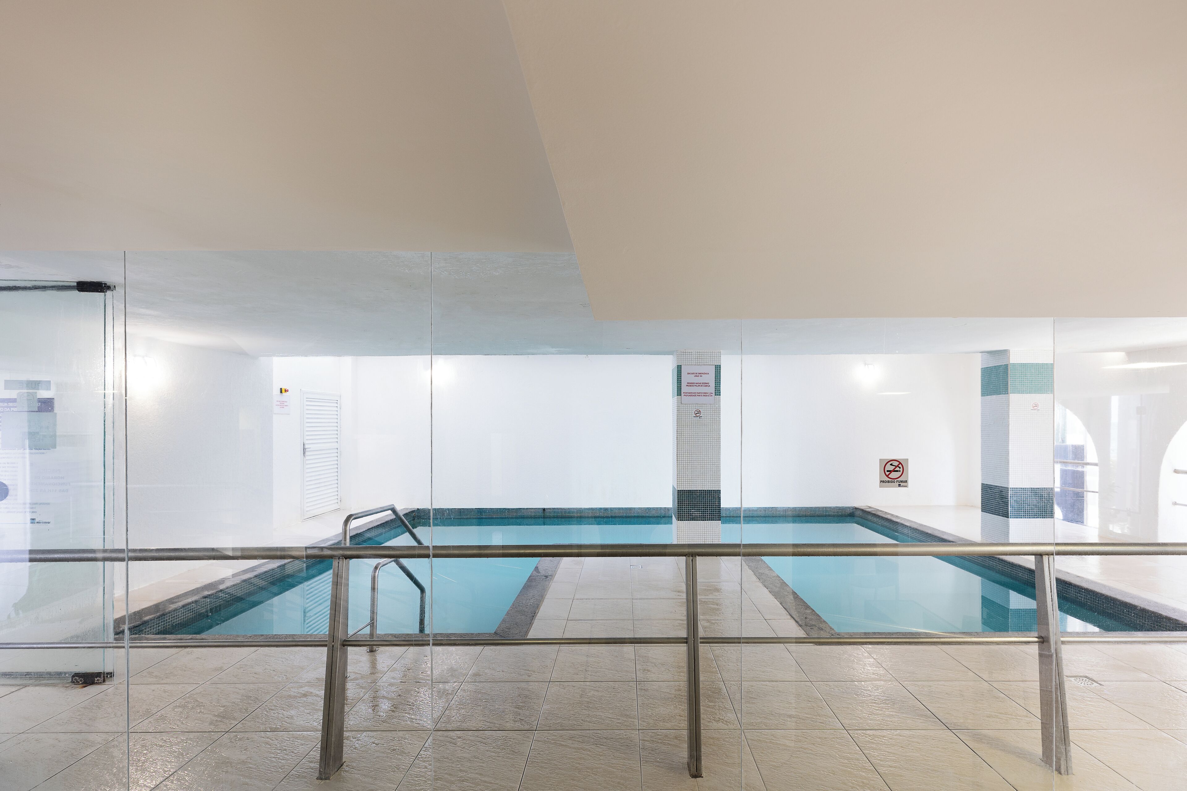 Una piscina interior con barreras de vidrio transparente, suelo y pared de azulejos.