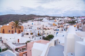 A coastal town with white buildings, a palm tree, and a mountainous backdrop.