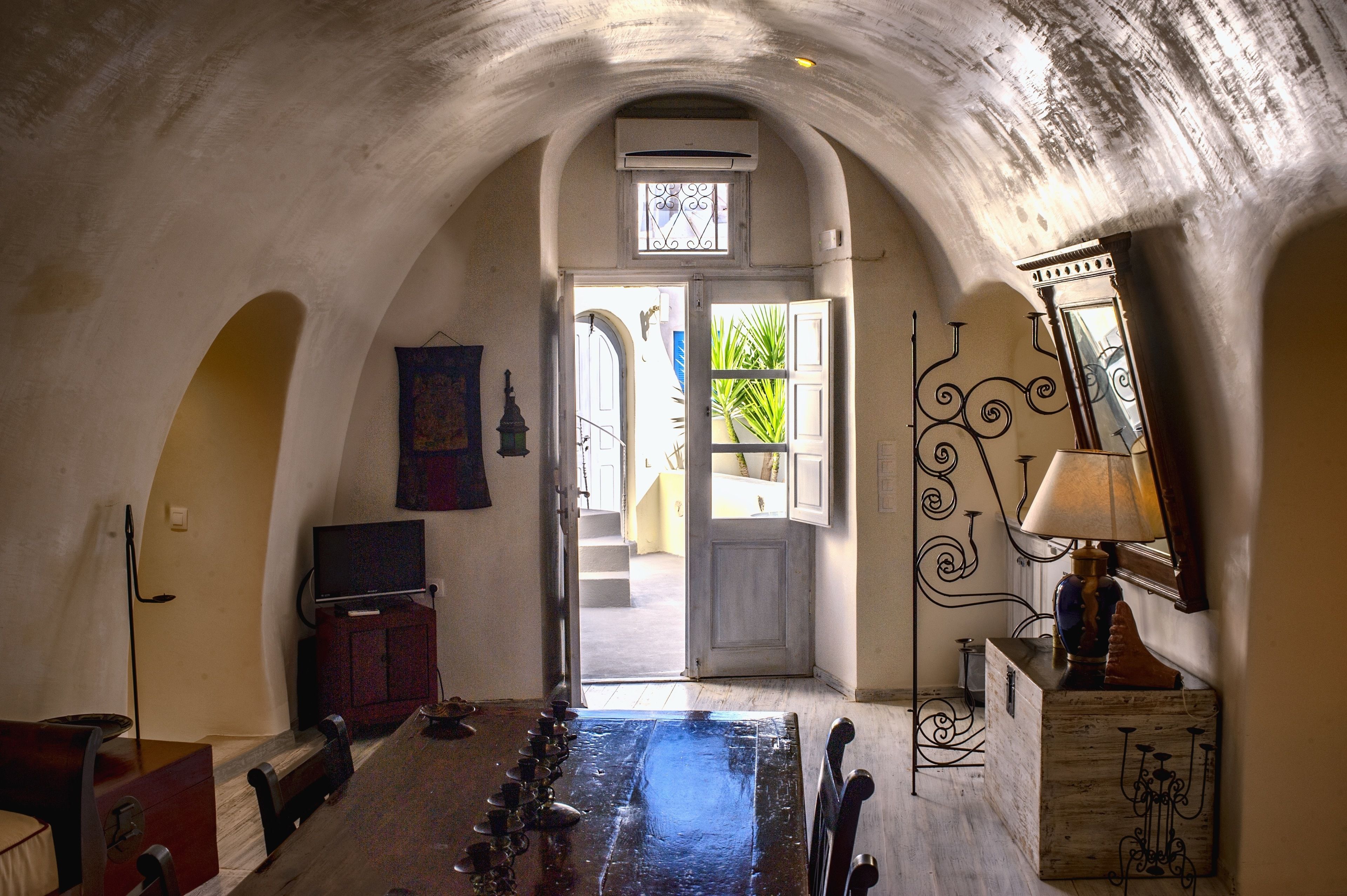 An arched hallway with a television, a wooden cabinet, and a candelabra.
