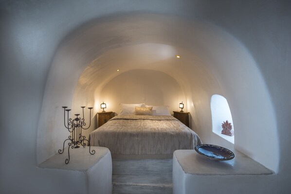 Un dormitorio acogedor con techo abovedado, una cama con colcha estampada, lámparas de noche y un candelabro decorativo.