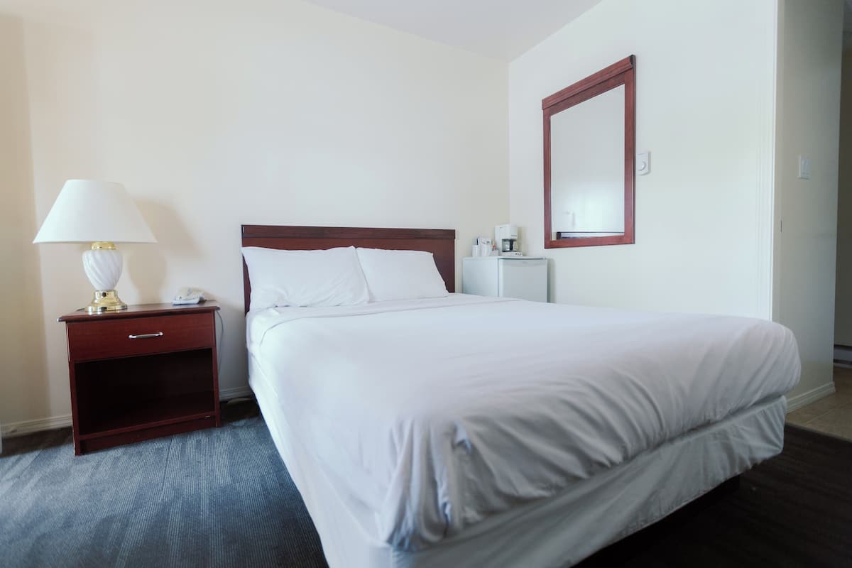 Un lit bien fait dans une chambre d’hôtel, avec une table de chevet en bois, une lampe et une petite table sur laquelle se trouve une machine à café.