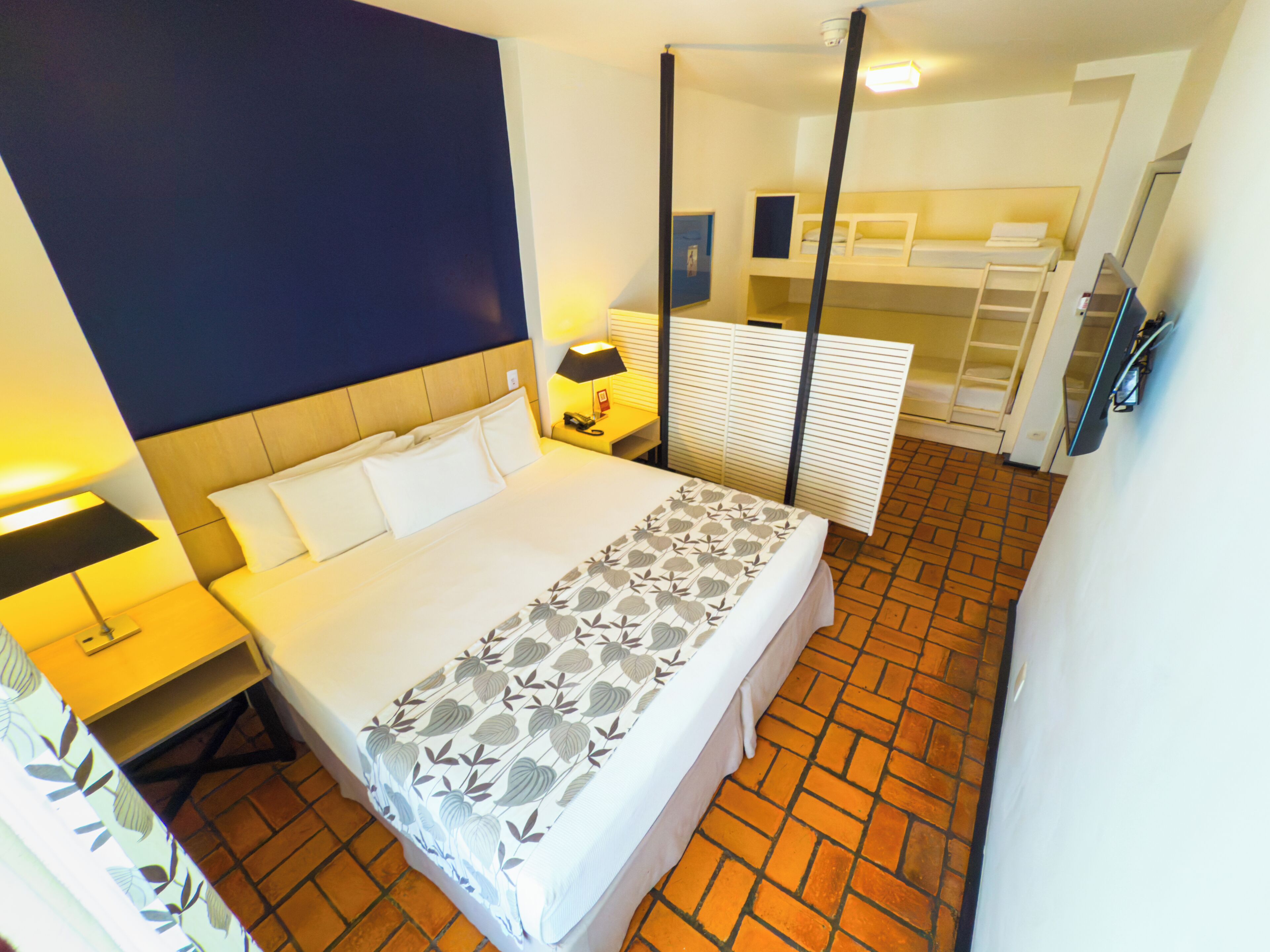 A hotel room with a large bed, a nightstand with a lamp, a wardrobe, and a bathroom with a shower and toilet.