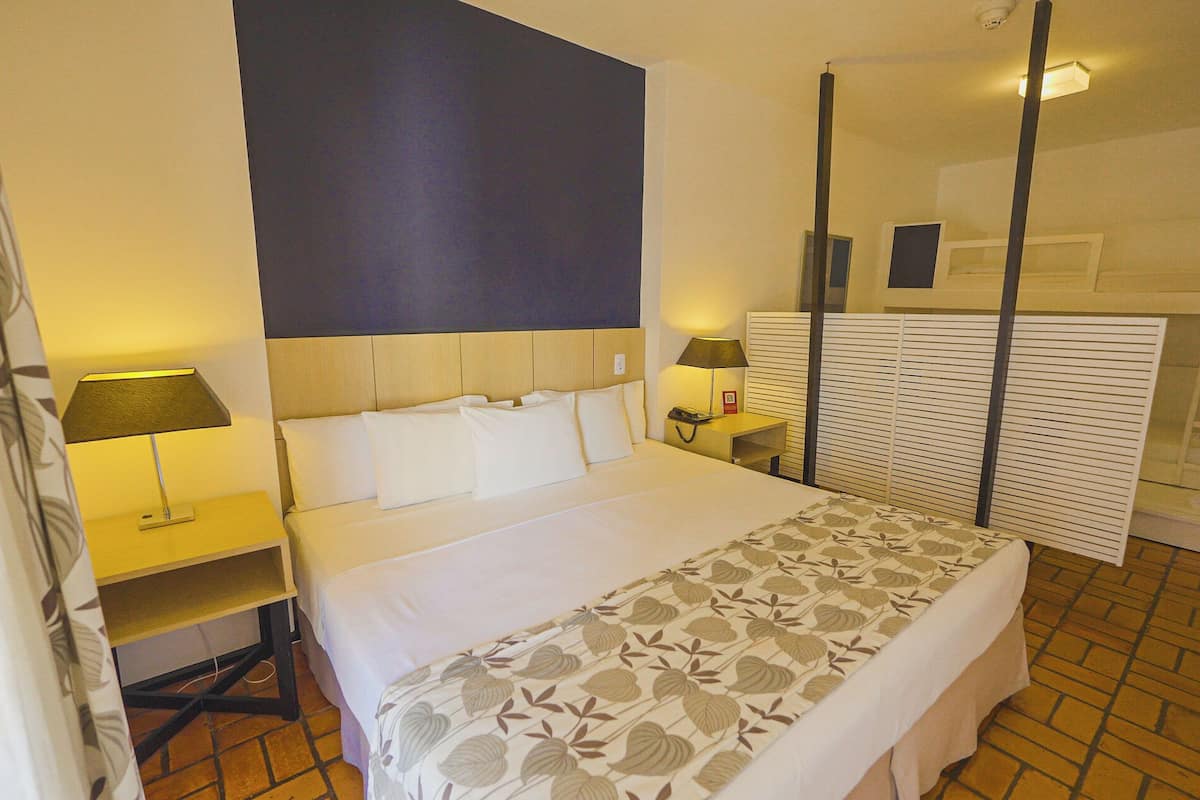 Una habitación de hotel con una cama, dos mesitas de noche con lámparas, un espejo y una colcha estampada.