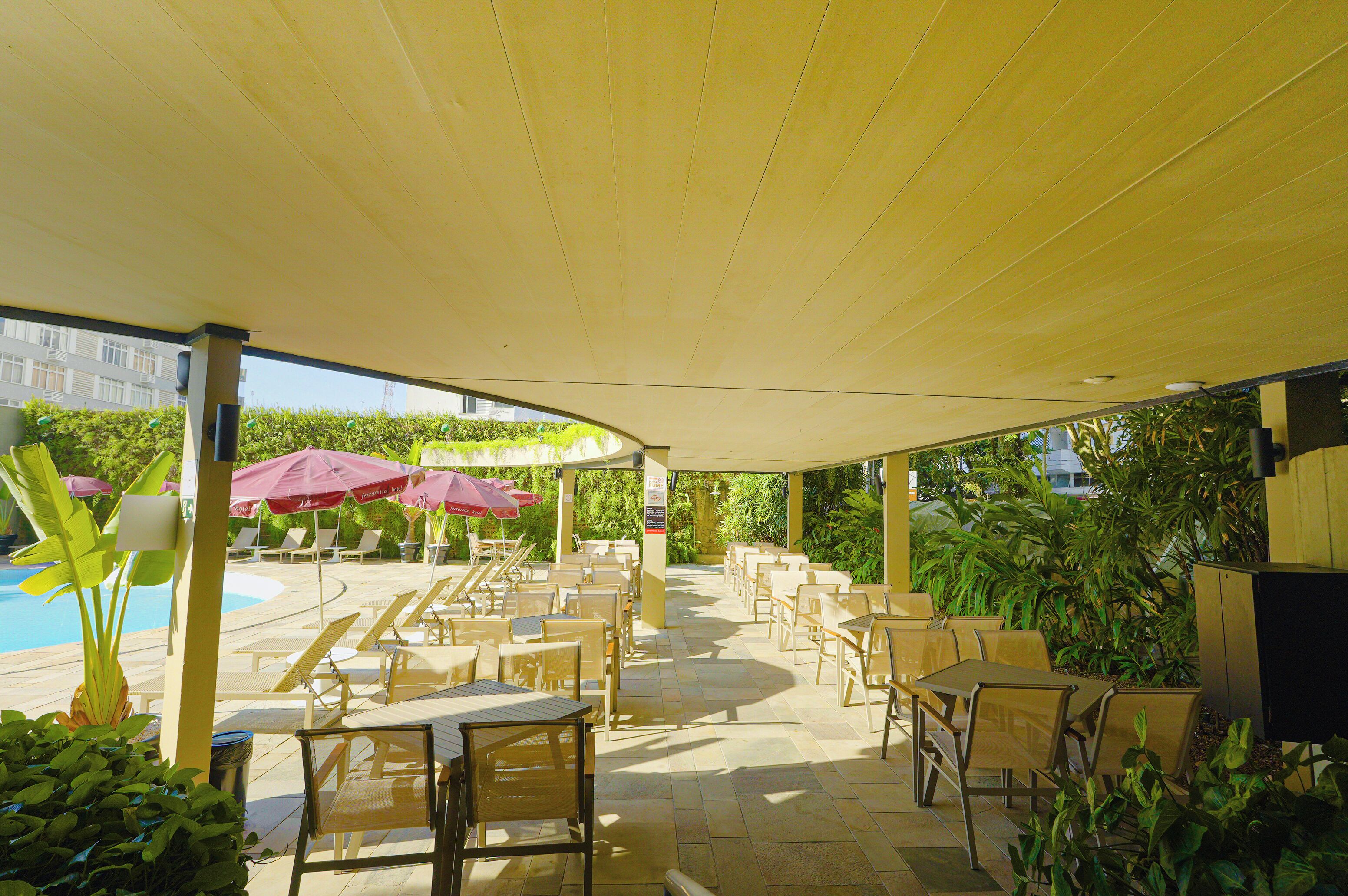 An outdoor patio area with sun loungers and tables, surrounded by greenery and a pool.