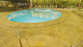 Piscina com deck revestido, rodeada por espreguiçadeiras e um bar.