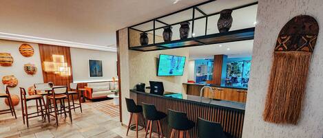 A modern kitchen with a bar area, wooden bar stools, and a television.