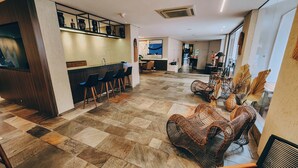 Eine großzügige Lobby mit Schachbrettmuster-Boden, einer Bar mit Hockern und Korbmöbeln.