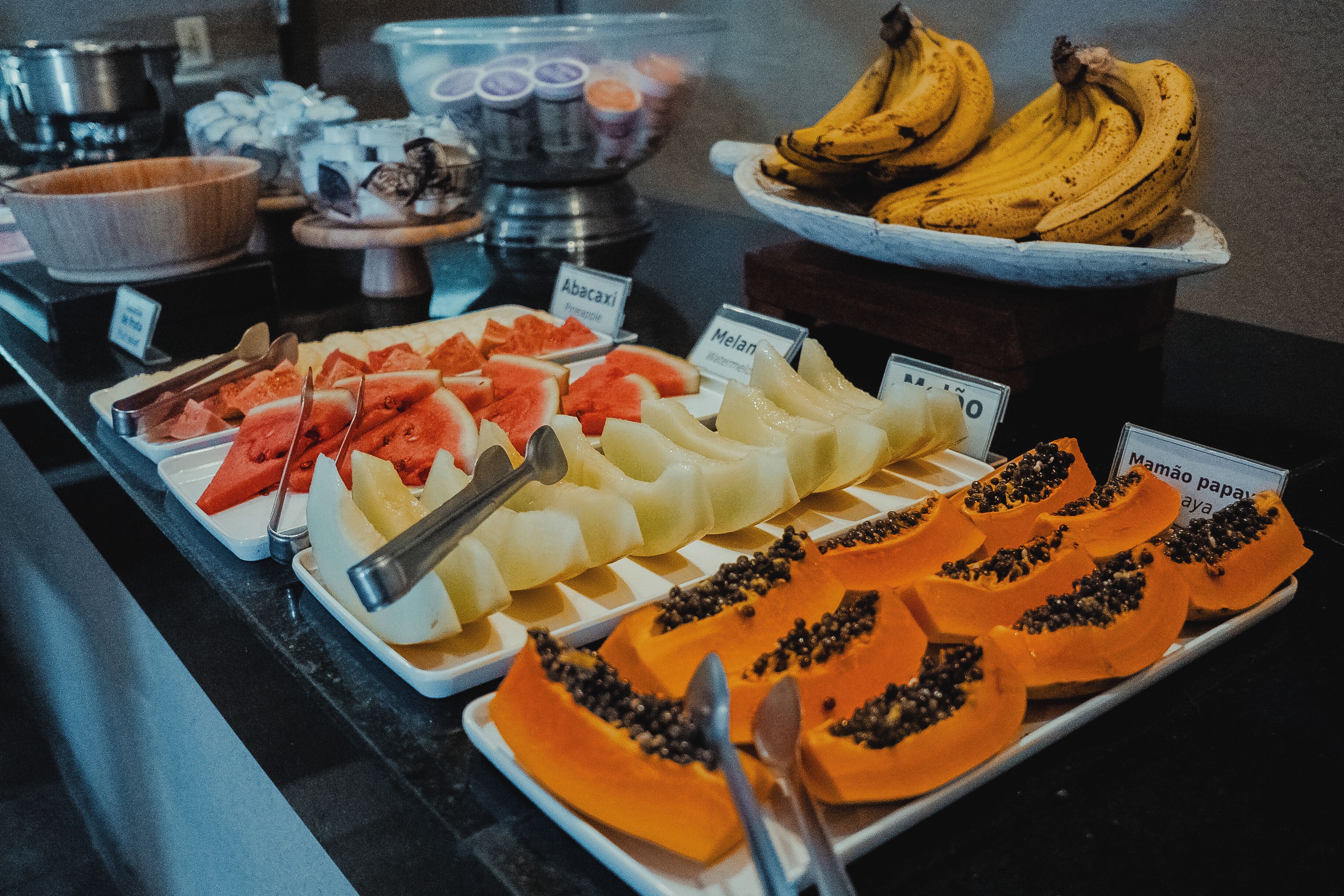 Buffet com diversas frutas e um letreiro mostrando o preço da mamão.