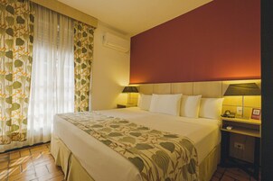 Habitación de hotel con cama, mesita de noche con lámpara, teléfono y aire acondicionado instalado en la pared.