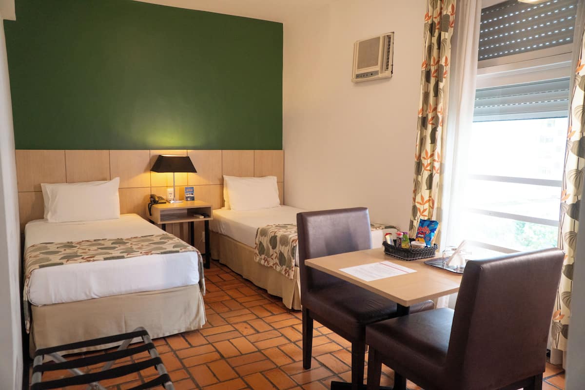 Una habitación de hotel con dos camas, un escritorio, una silla, una lámpara y una ventana con cortinas.