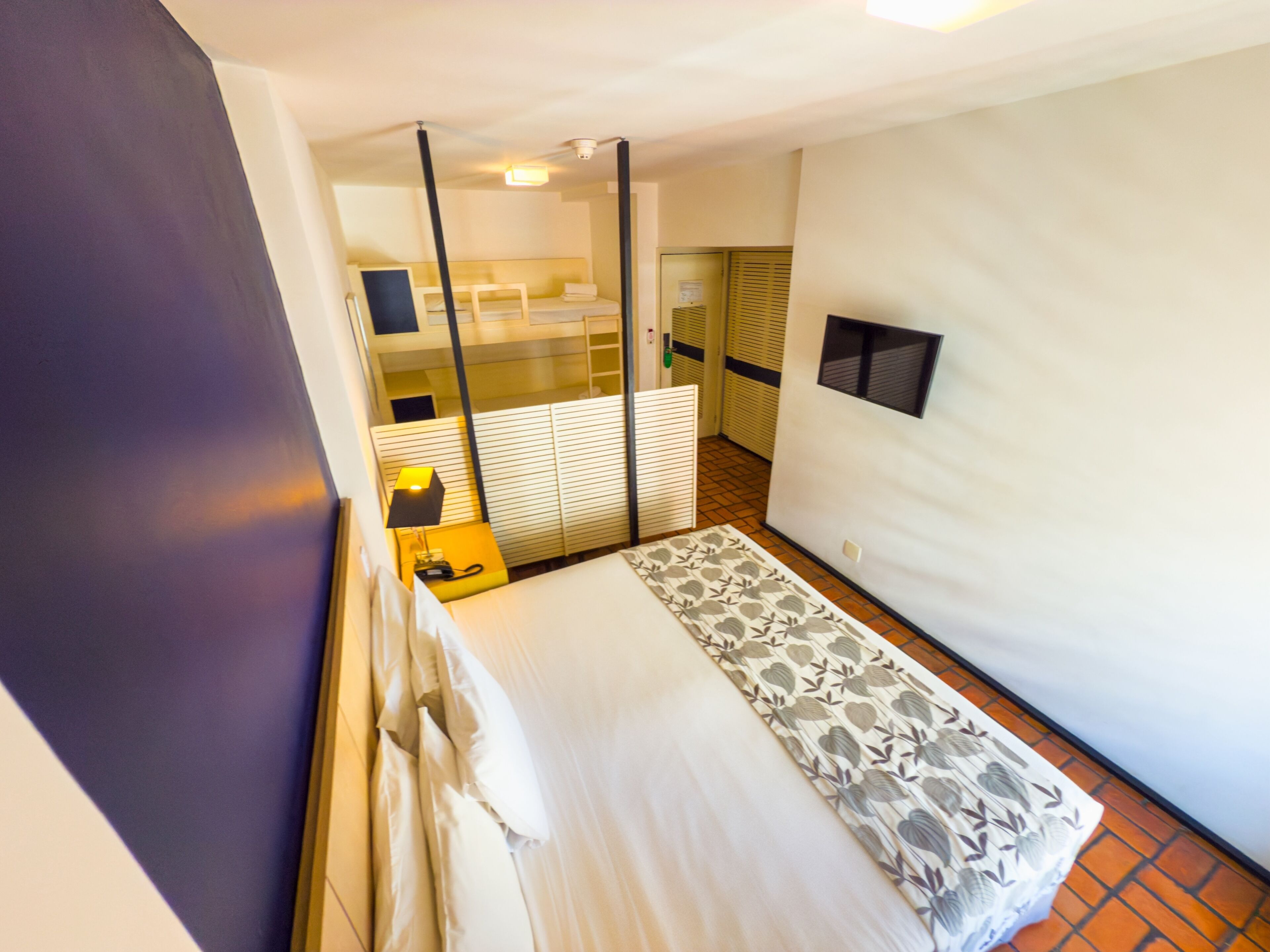 A hotel room with a bed, a bedside table with a lamp, a mirror, and a window.