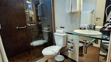 A modern bathroom with a glass shower enclosure, a white toilet, a glass sink, and a mirror.