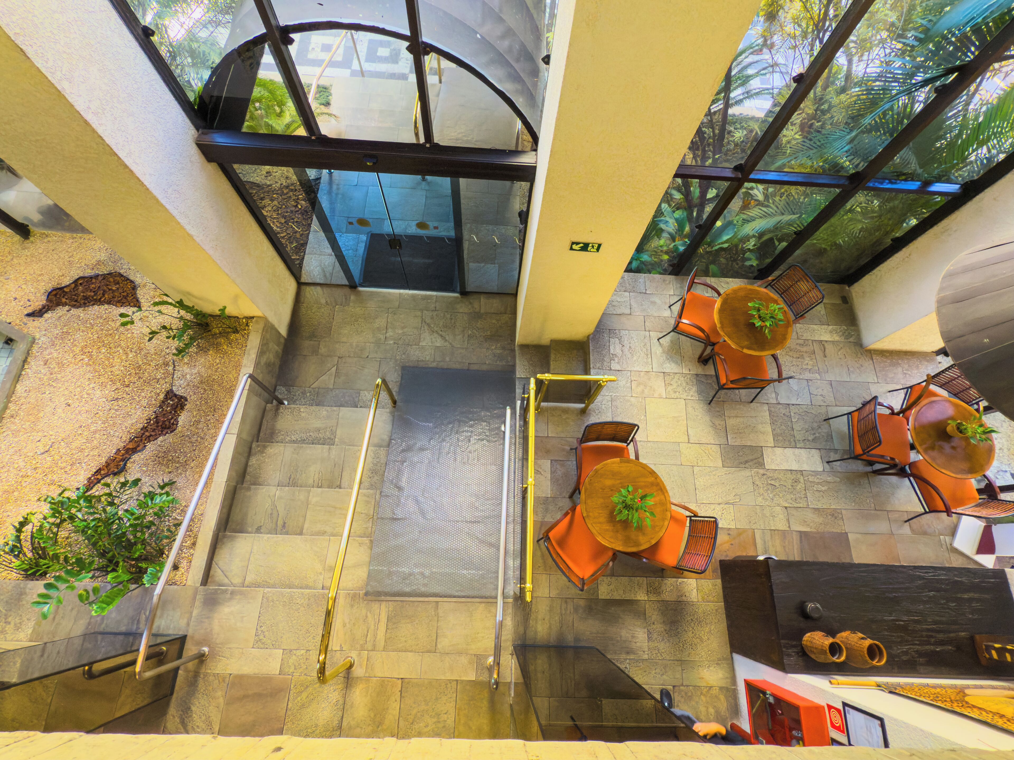 An upper-level view of a hotel lobby with a glass ceiling, outdoor seating area, and a staircase.