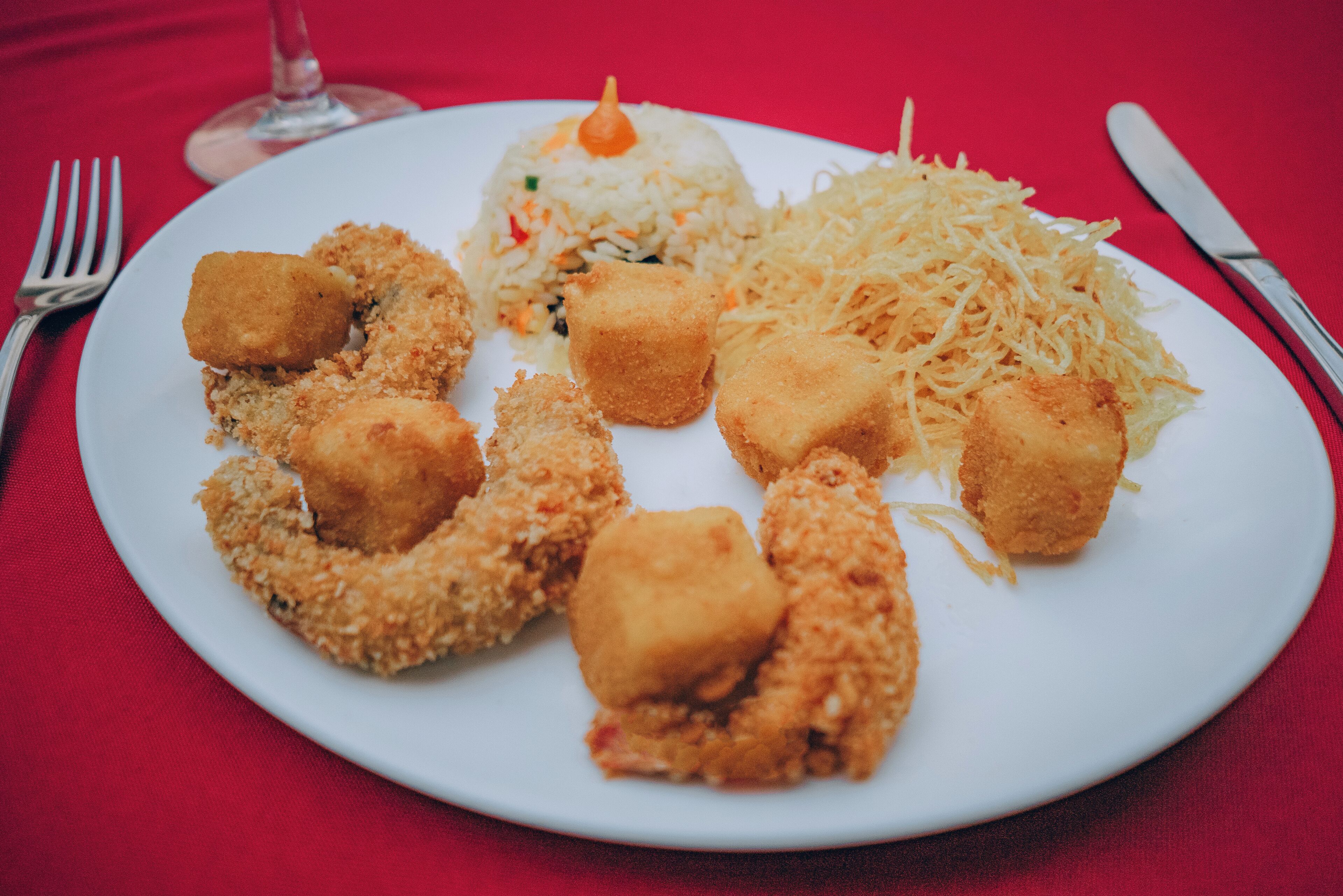 Un plato con comida frita y una copa de vino sobre un mantel rojo.