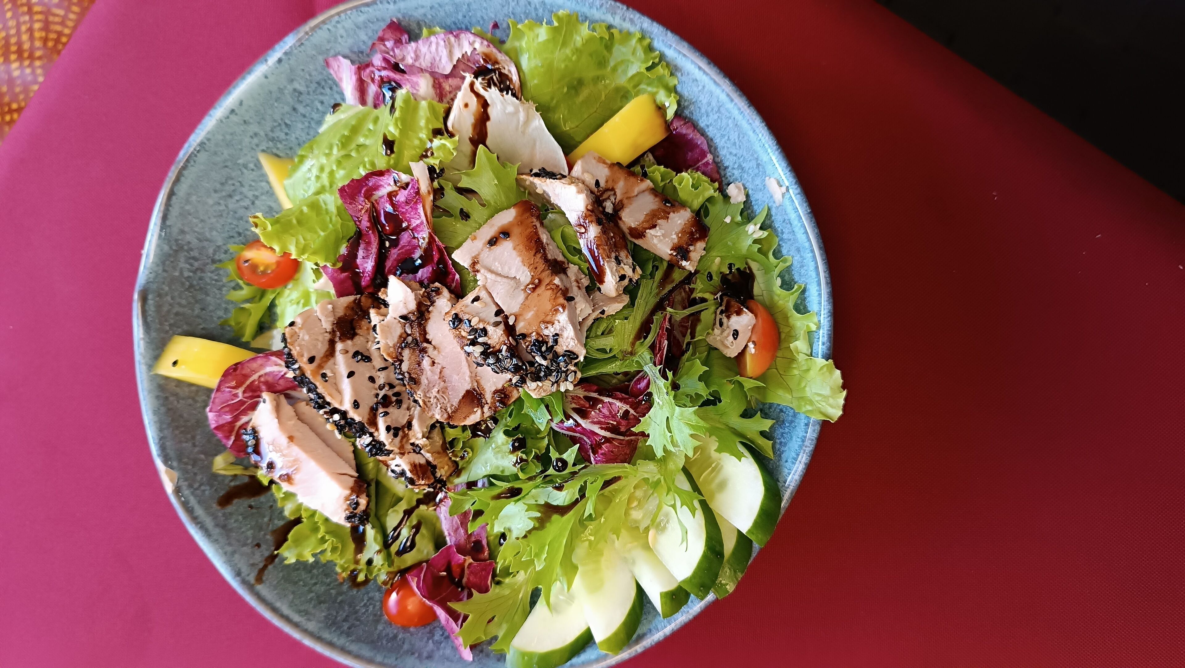 A plate of mixed greens and sliced chicken with sesame seeds.