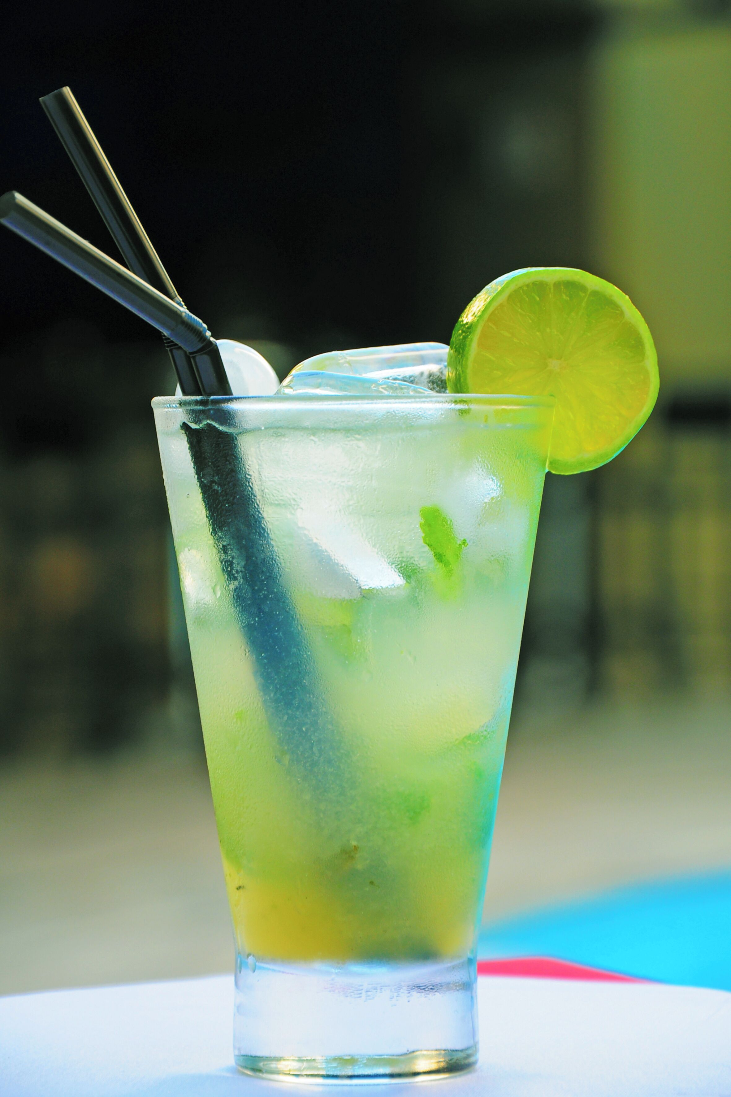 A tall glass with a lime slice and a straw, filled with a greenish drink and ice cubes.