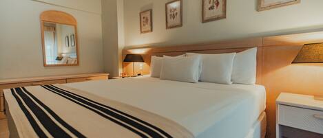 A hotel room with a large bed, a bedside table with a lamp, a nightstand, and framed pictures on the wall.