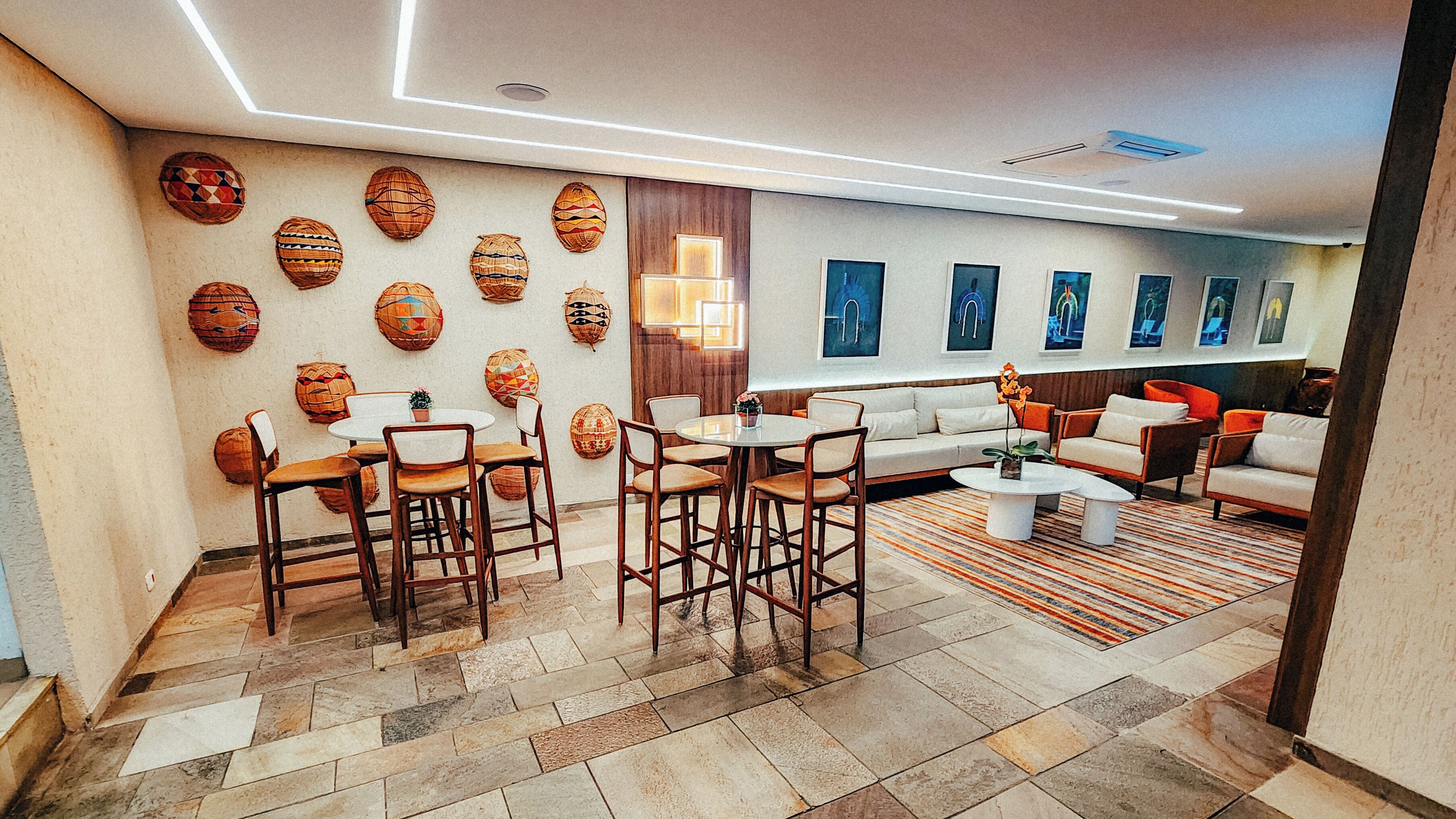 A modern living room with a sofa, chairs, a coffee table, and a dining area with chairs and a table. There are decorative woven baskets on the wall and a rug on the floor.