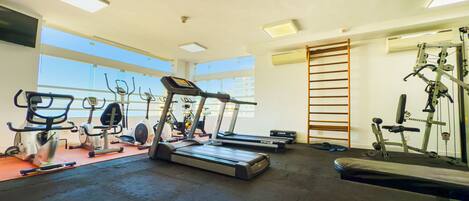 A gym with various exercise equipment, large windows, and a high ceiling.