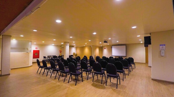 A conference room with rows of chairs, a whiteboard, and a projector screen.