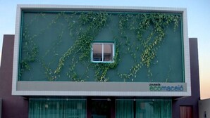 A modern building with a large glass facade, a green wall with climbing plants, and a sign reading "pousada ecolacio". - Pousada Ecomaceio (Maceió)