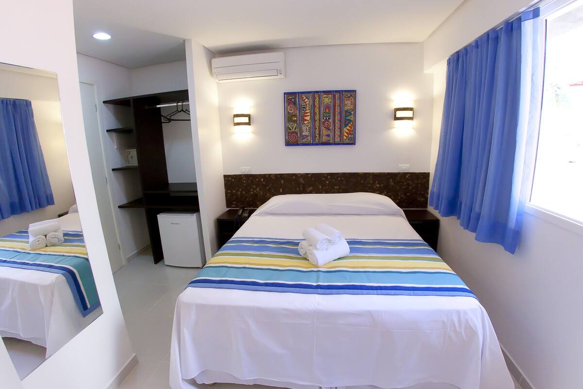 A hotel room with two beds, a desk, a wardrobe, and a small kitchenette.