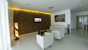 A modern lobby with a flat-screen TV, a textured wall, white sofas, and a large painting. - Pousada Ecomaceio (Maceió)