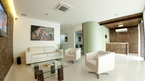 A modern living room with a white sofa, a glass coffee table, and a beige armchair. There is a painting on the wall and a television on the left. - Pousada Ecomaceio (Maceió)