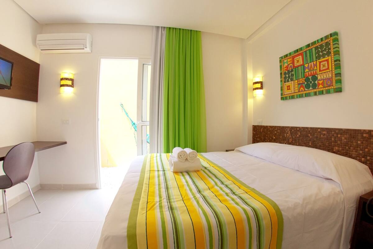 A hotel room with a bed, a desk, a chair, a TV, and a painting on the wall.