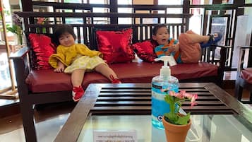 A seating area with a glass table in front, a bottle of hand sanitizer, and a sign with Thai text.
