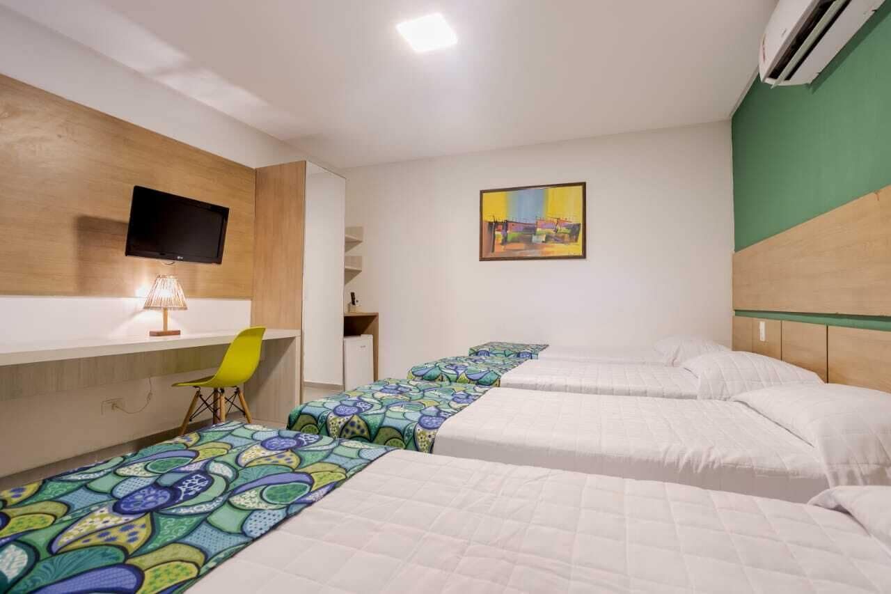 Habitación de hotel con tres camas, un escritorio con silla, televisión y un cuadro en la pared.