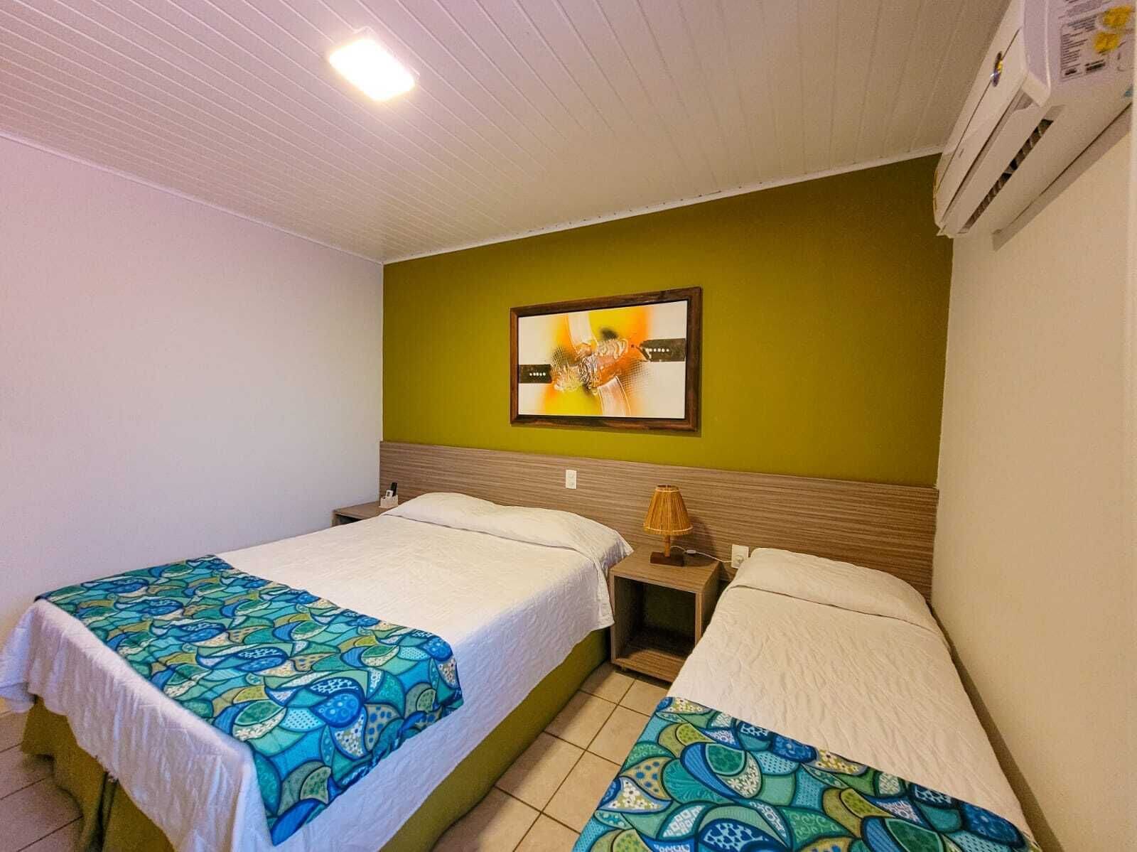 Een hotelkamer met twee bedden, elk met een gebeddelen sprei, een nachtkastje met een lamp en een ingelijst schilderij aan de muur.