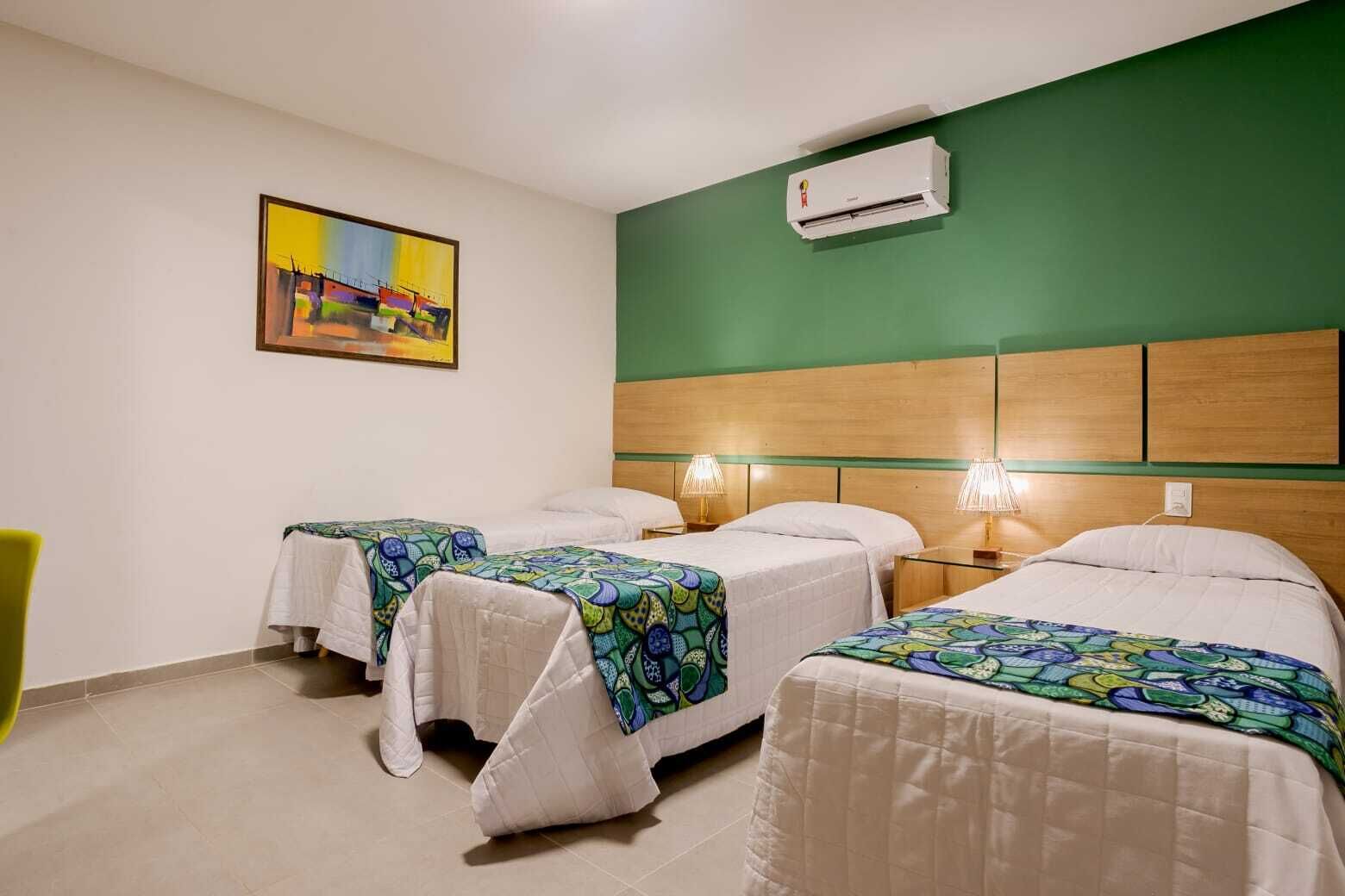 Une chambre d’hôtel avec deux lits, un mur vert, un climatiseur et un tableau.