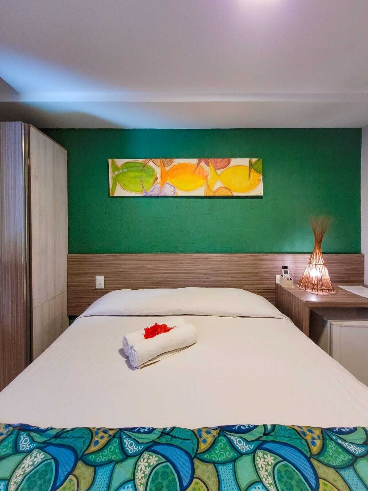 A hotel room with a bed, a green wall, and a painting of fish.