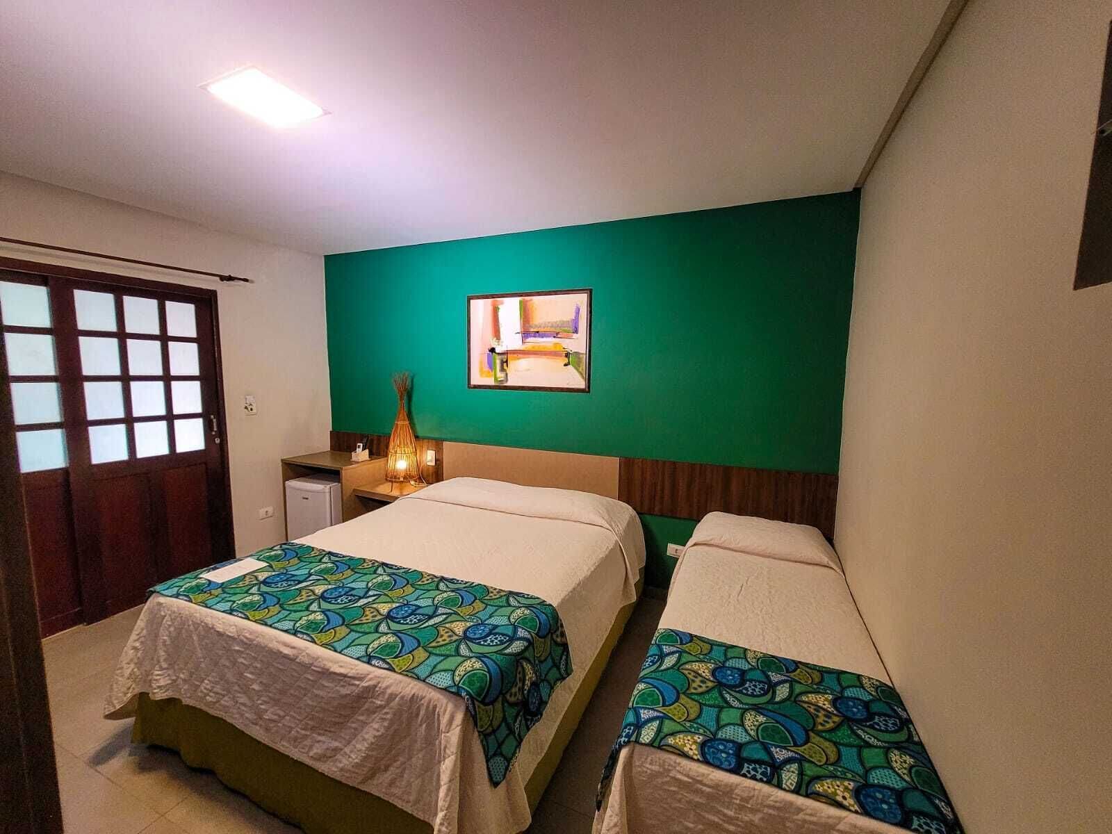 Una camera d'albergo con due letti, una scrivania, una sedia, un tavolino, una lampada e un quadro appeso al muro.