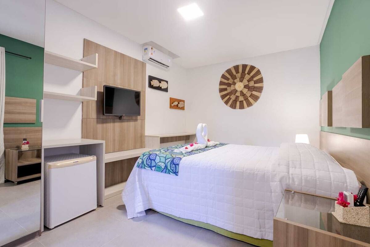 Hotellihuone, jossa on sänky, työpöytä, televisio, tikanheittoalusta ja minibaari.