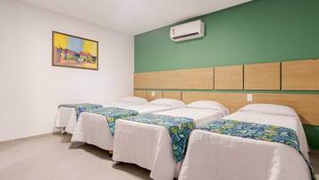 A hotel room with three single beds, a green wall, an air conditioning unit, and a colorful painting on the wall.