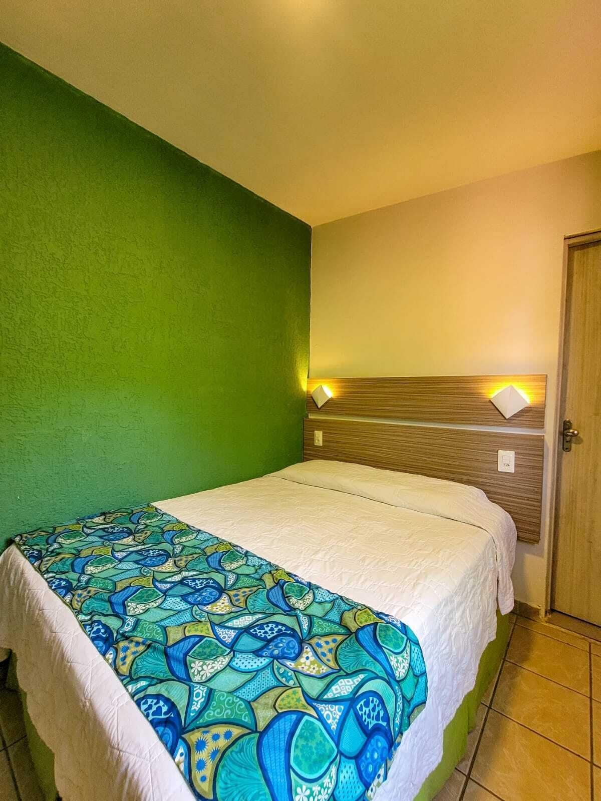 A single bed with a patterned bedspread, a wooden headboard with wall-mounted lights, and a green wall.
