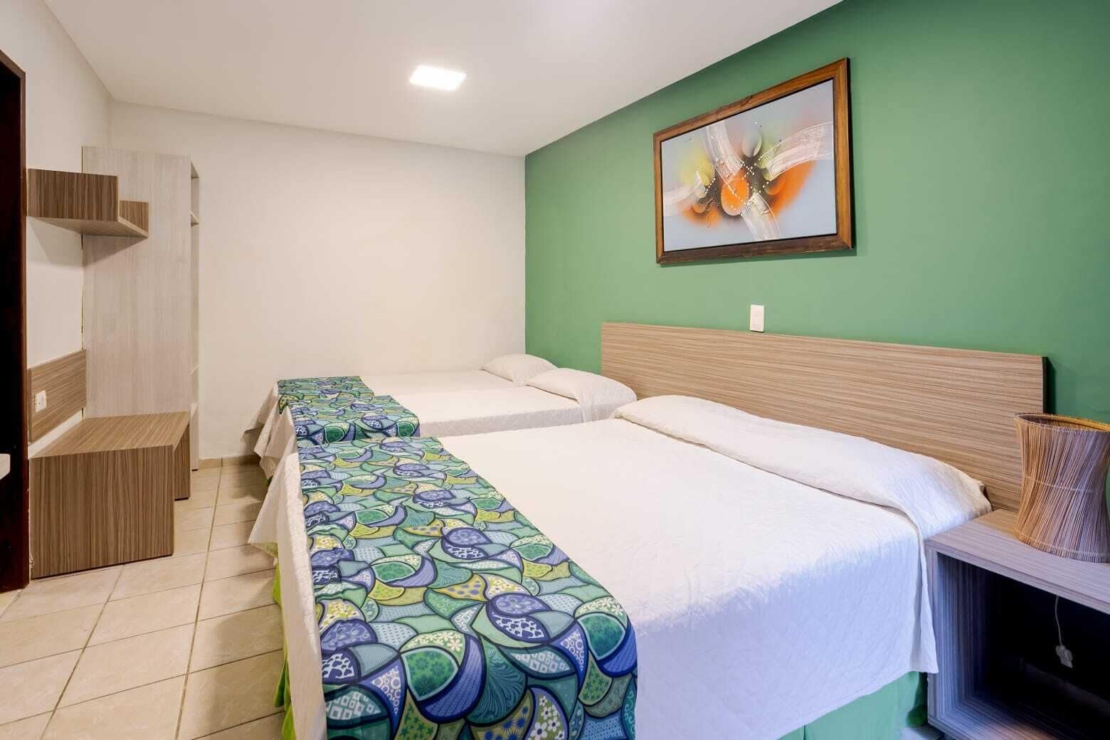 A hotel room with two single beds, a wooden bench, a green wall, and a framed abstract painting.