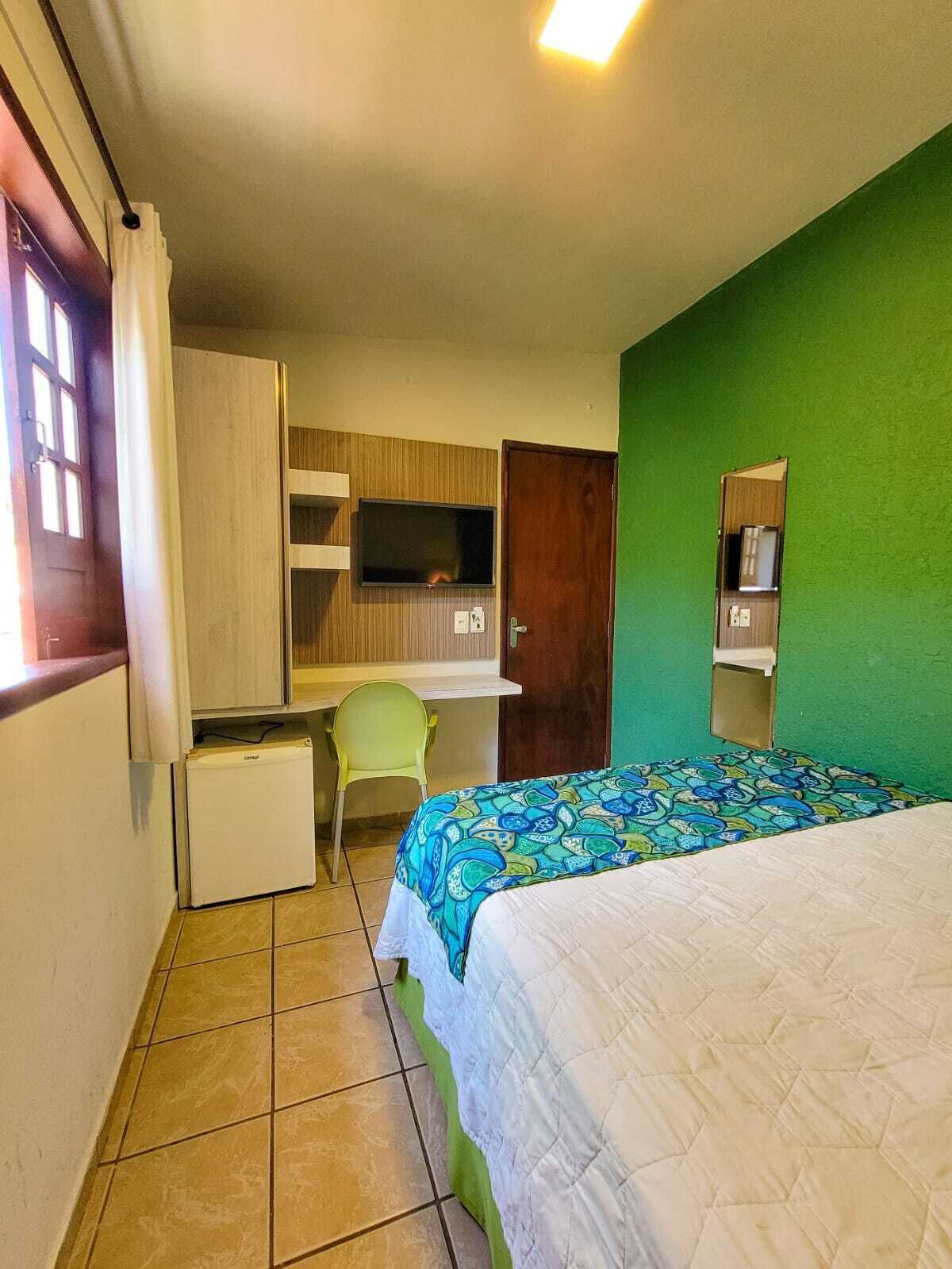Una camera da letto con un letto, una scrivania, una sedia, una televisione e un muro verde.