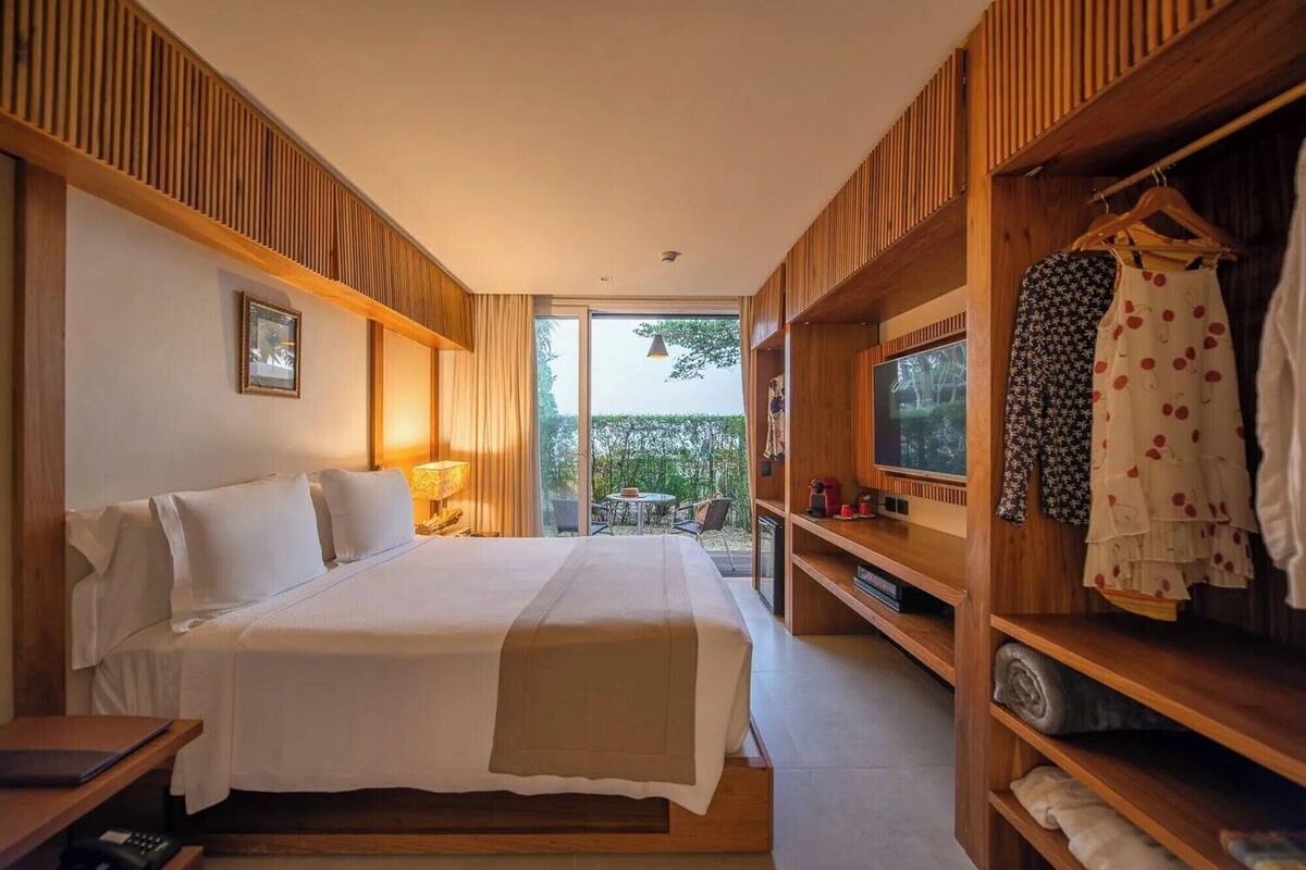 A hotel room with a bed, a TV, a wardrobe, and a view of the outdoors.