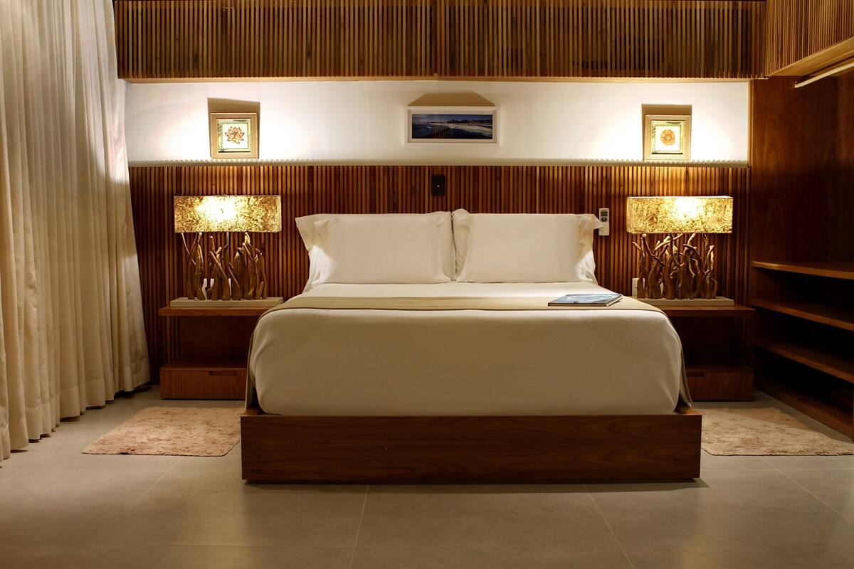 A modern bedroom with a large bed, wooden paneling on the walls, two bedside tables with lamps, and a small framed picture above the bed.