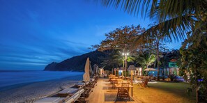 A beachside resort with outdoor seating, palm trees, and a view of the ocean at dusk. - Hotel Spa Nau Royal (São Sebastião)