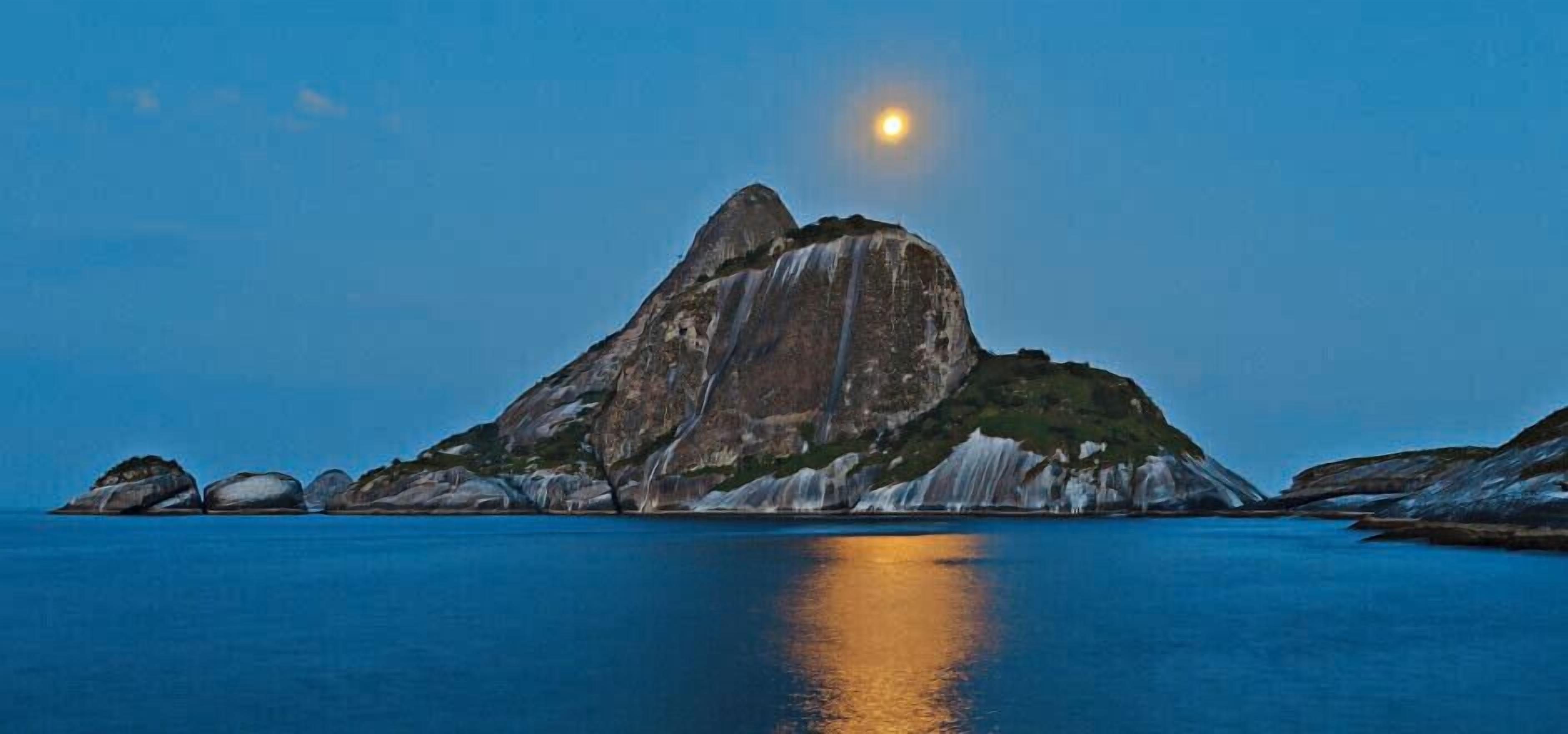 A mountain with a reflection in calm water under a clear sky.