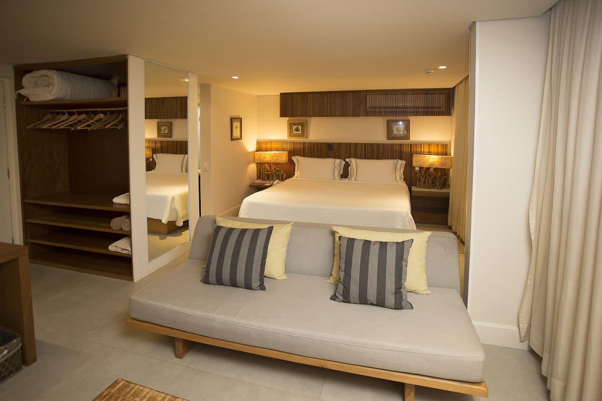 A hotel room with a bed, a sofa, a wardrobe, and a mirror.