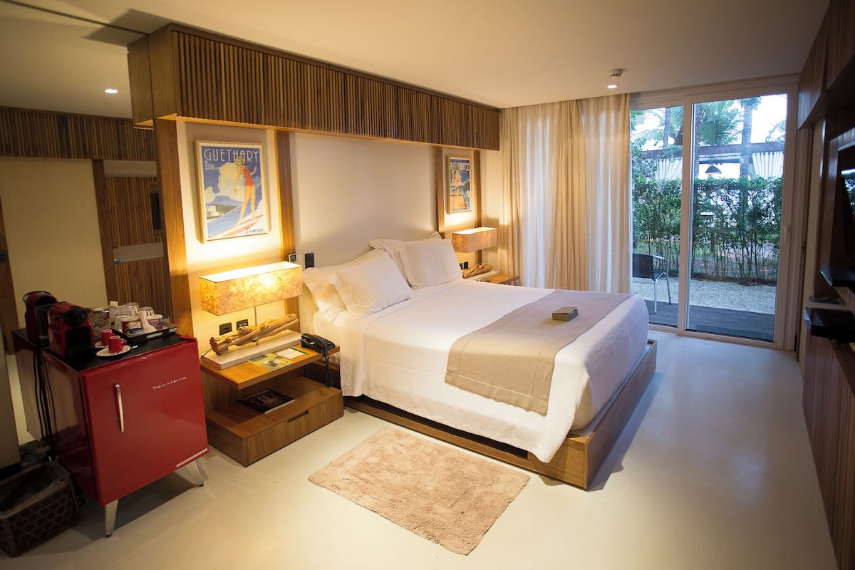 A hotel room with a large bed, a desk with a lamp, a red minibar, and a view of the outdoors.